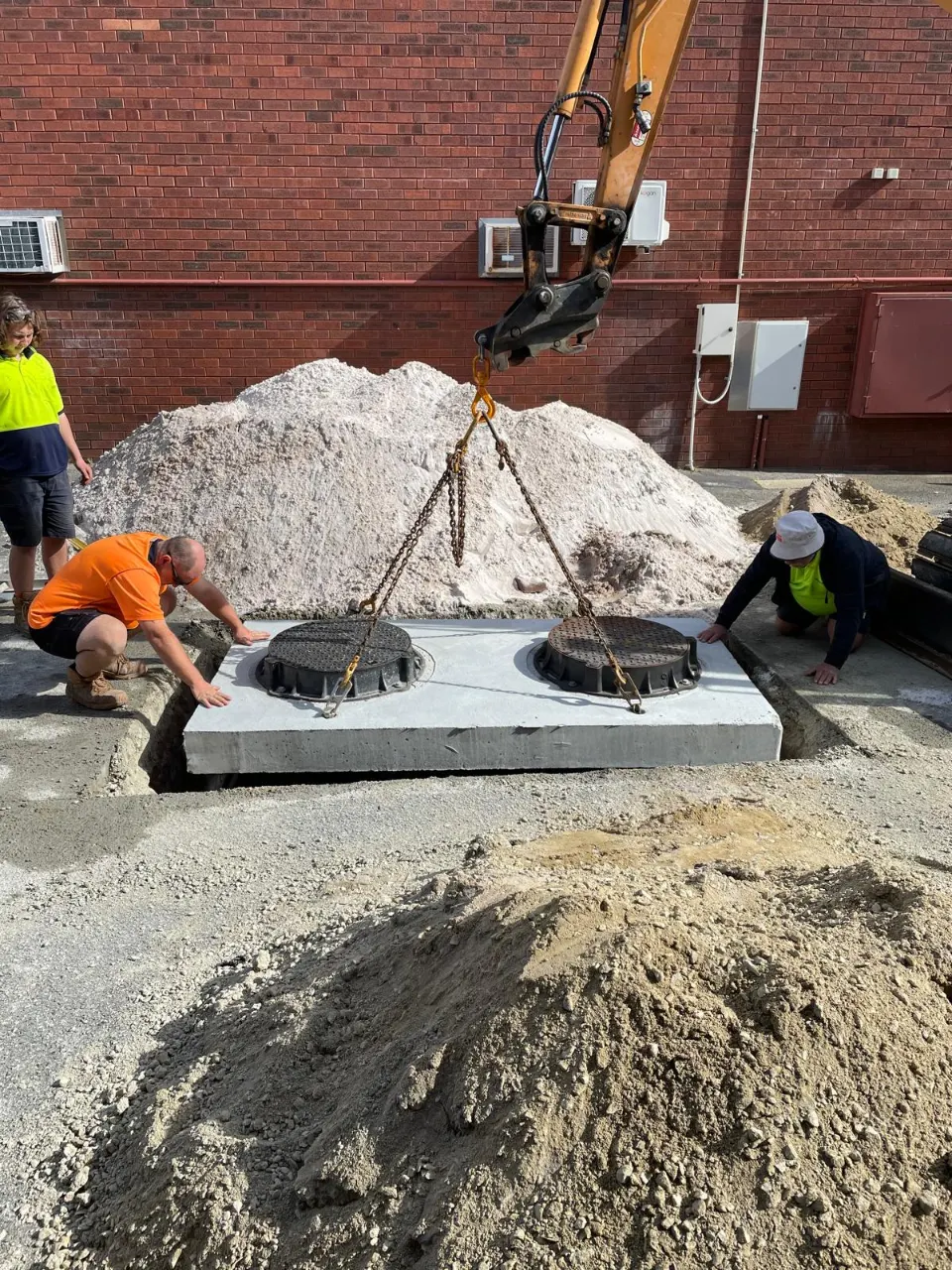 Precast concrete pit with two lids being lowered into position by crane, with workers guiding it
